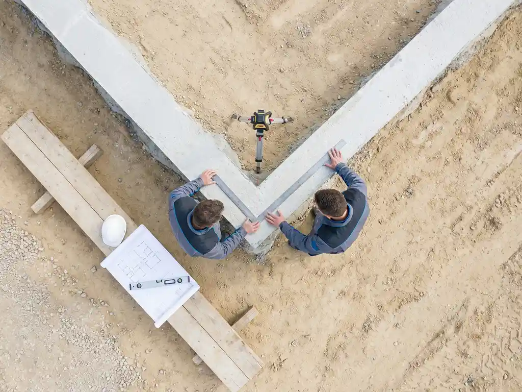 Betonnen funderingshoek wordt onderzocht met professionele meetgereedschappen in minimalistische bouwomgeving