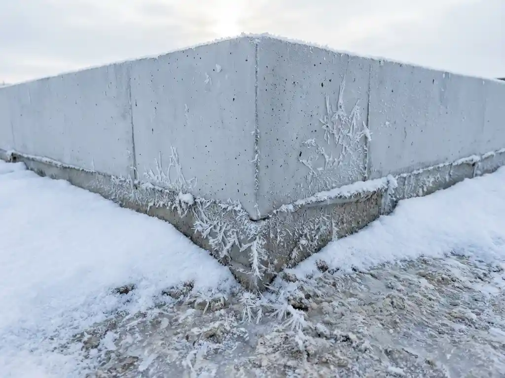 Betonnen fundering hoek met ijskristallen en vorst patronen op glad oppervlak, omringd door witte sneeuw