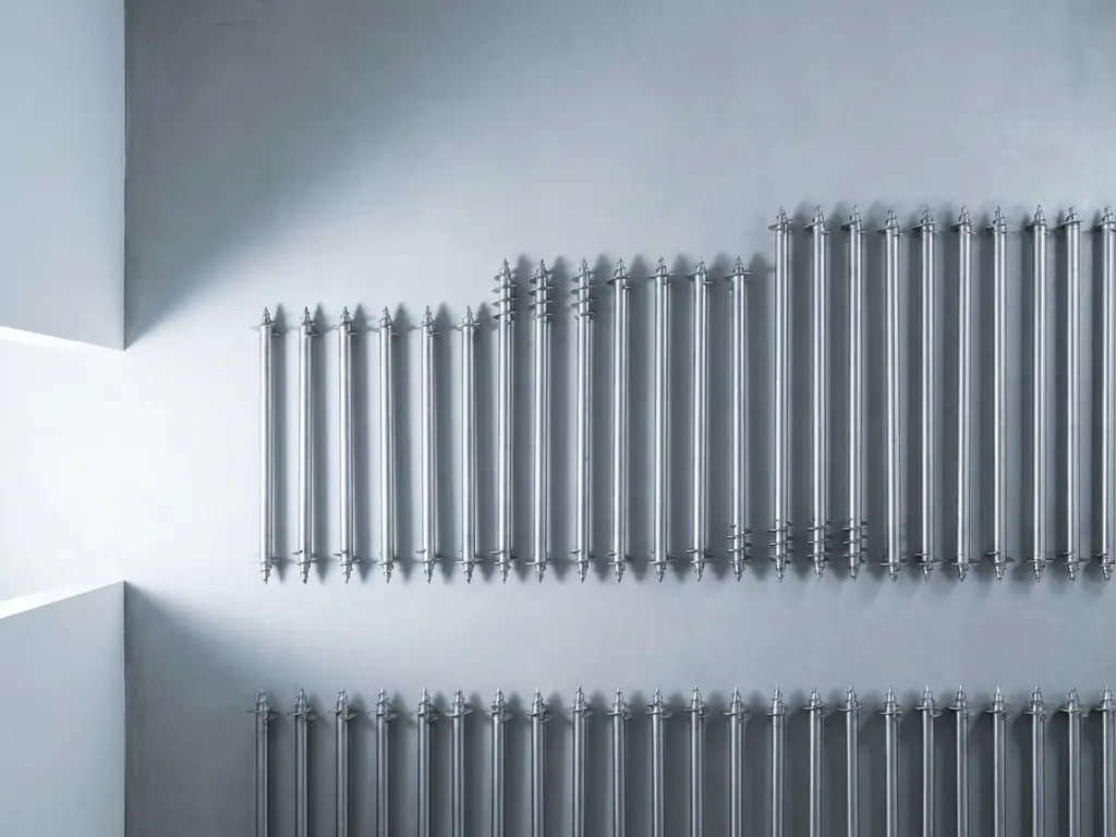 krinner-schroefpalen-metaal-industrieel-minimalistisch.jpg Krinner schroefpalen in verschillende lengtes gerangschikt op betonnen ondergrond met spiraalvormige schroefdraad