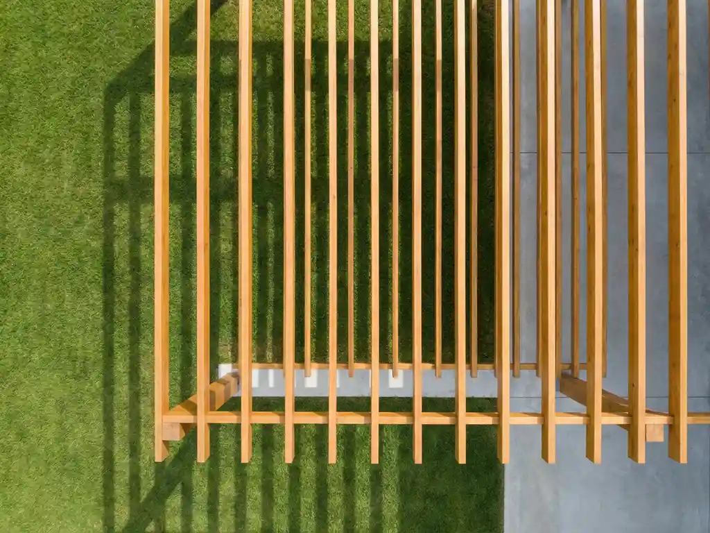 Houten pergola met geometrische balken op eigendomsgrens, betonnen fundering en gemaaid gazon in minimalistische stijl