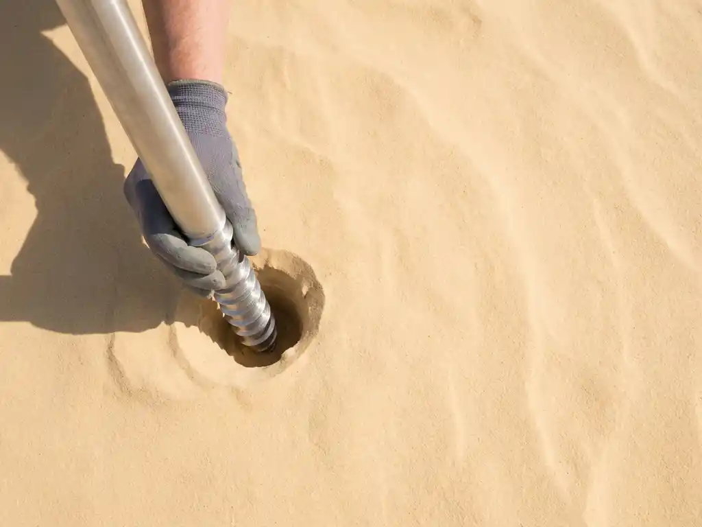 Stalen schroeffundatie paal wordt gepositioneerd in gouden zandgrond, geometrische spiraaldraden vangen natuurlijk licht