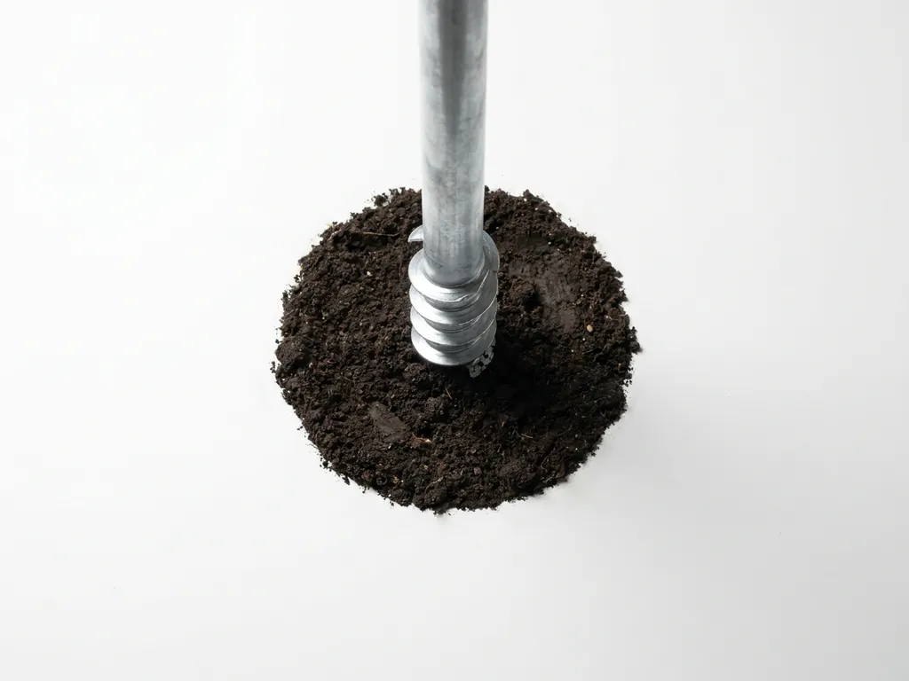 schroefpaal-galvanisch-staal-grond-installatie.jpg Gegalvaniseerde stalen schroefpaal met spiraalvormige schroefdraad wordt in donkere grond geïnstalleerd, bovenaanzicht