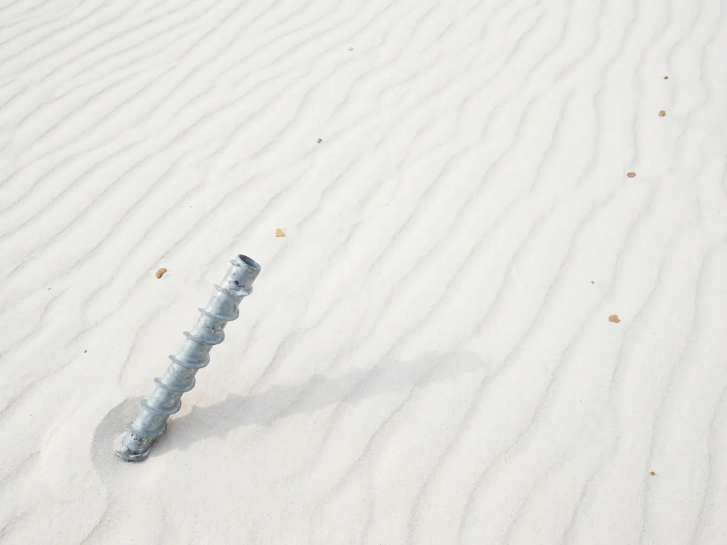 Gegalvaniseerde stalen schroefpaal in wit zand met helixvormige draden die zachte schaduwen werpen