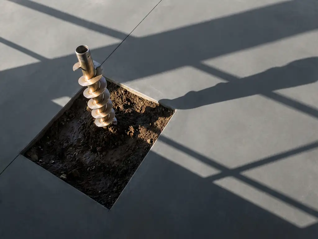 Stalen schroefpaalfundering met spiraalvormige draad in donkere grond, gezien vanuit vogelperspectief met geometrische schaduwen