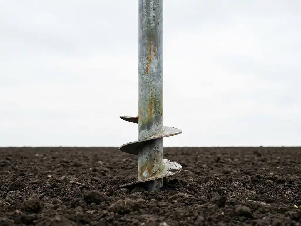 Verweerde stalen schroefpaal verticaal geplaatst in donkere grond met gegalvaniseerd oppervlak en subtiele patina