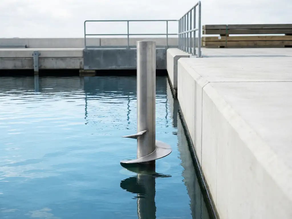 schroefpaal-fundatie-water-constructie-staal.jpg Stalen schroeffundatiepaal met spiraalbladen onder water bij betonnen kade, industriële waterbouwconstructie